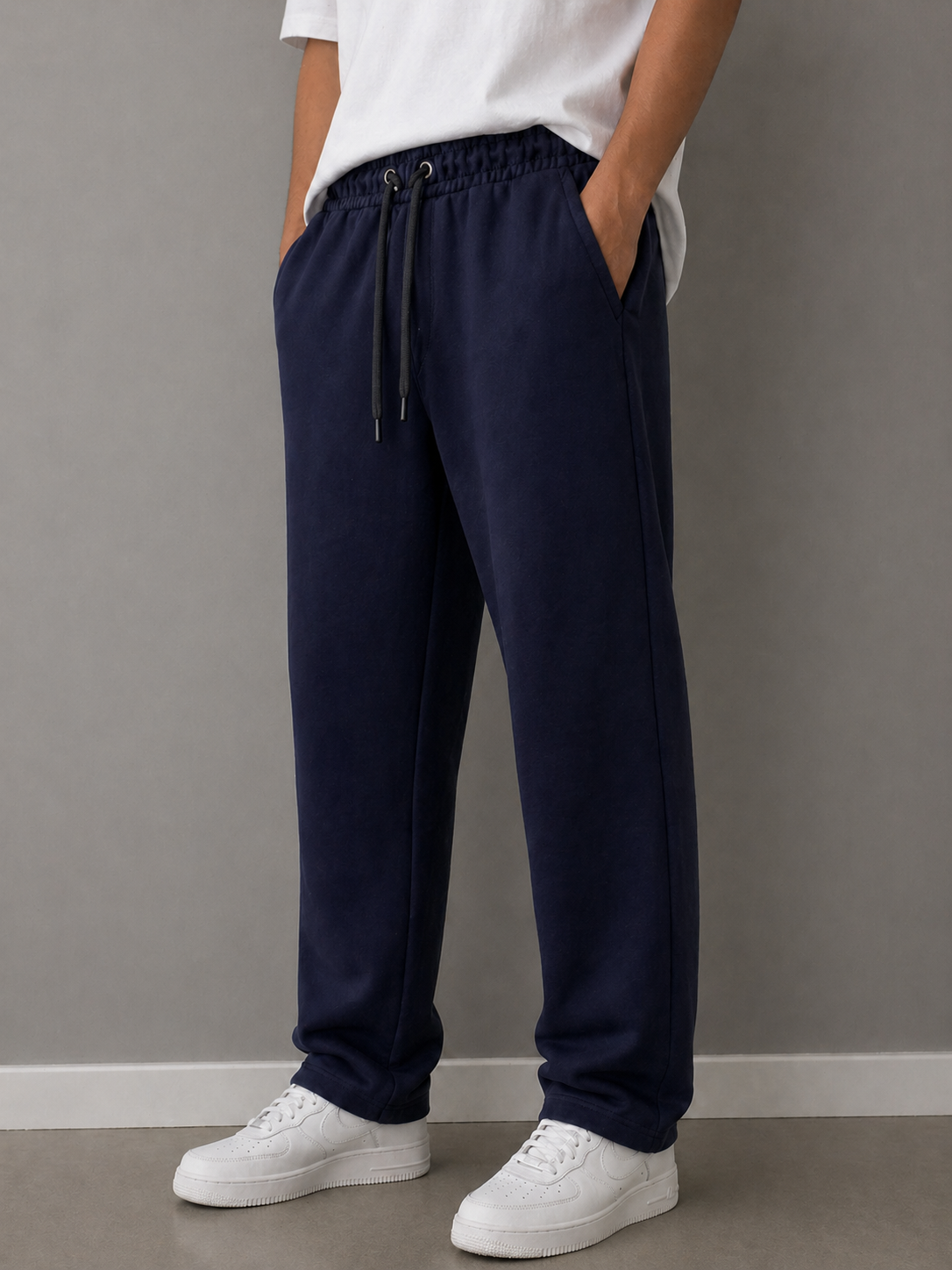 Person wearing navy blue pants and white sneakers against a gray wall.